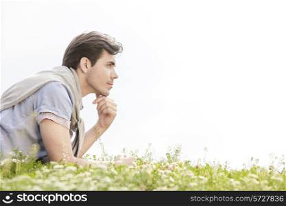 Side view of thoughtful young man lying on grass against clear sky