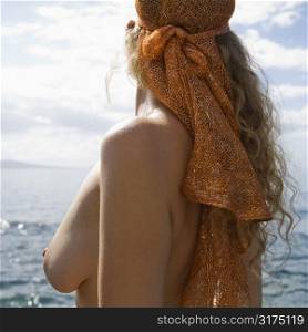 Side view of topless Caucasian mid-adult woman with wavy hair and head scarf at coast.