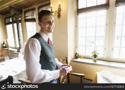 Side view of waiter with notepad smiling in restaurant