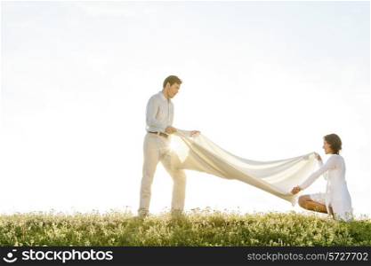 Side view of woman and man spreading picnic blanket on grass during sunny day