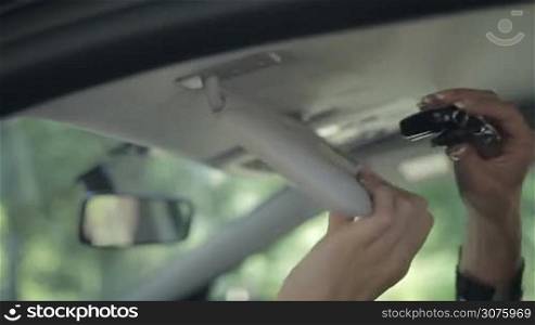 Side view of woman hand hiding ignition key in car sun visor
