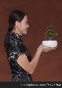 Side view of woman in traditional clothing holding a small plant in a flower pot, studio shot