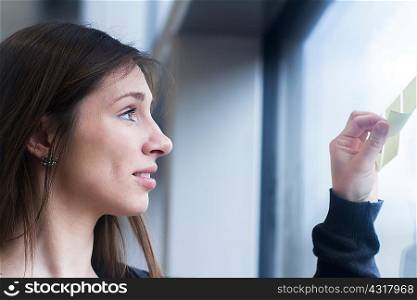 Side view of woman looking at adhesive notes stuck on window