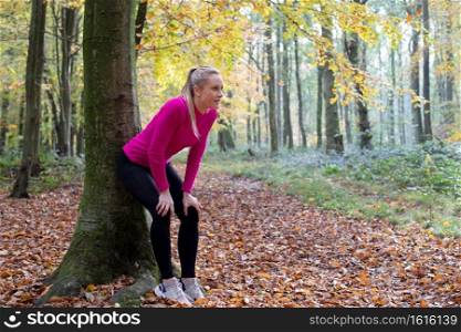 Side View Of Woman On Early Morning Autumn Run Through Woodland Resting After Exercise