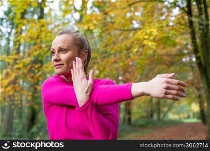 Side View Of Woman On Early Morning Autumn Run Through Woodland Stretching After Exercise