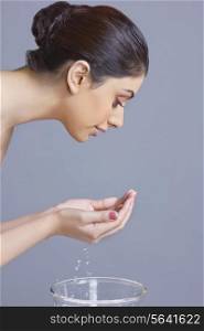 Side view of woman washing face with water against blue background