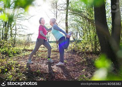 Side view of women in forest face to face holding ankle stretching leg