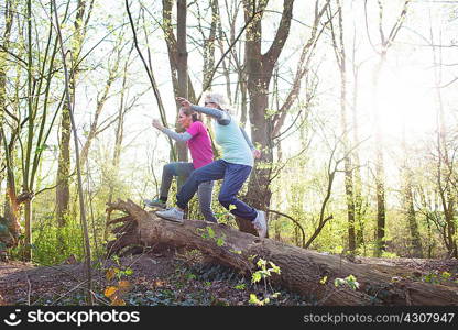 Side view of women in forest jumping over fallen tree