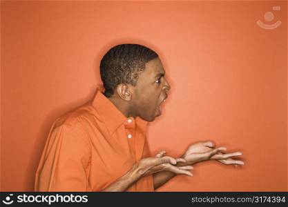 Side view of young African-American man on orange background expressing anger towards unseen person.