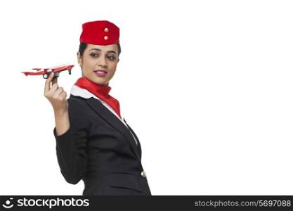 Side view of young airhostess holding toy airplane over white background
