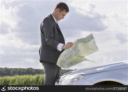 Side view of young businessman reading map by car at countryside