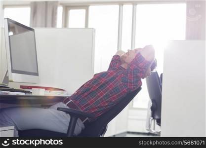 Side view of young businessman relaxing at computer desk in office
