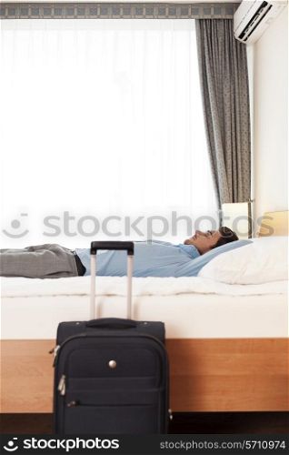 Side view of young businessman sleeping in bed by luggage at hotel room