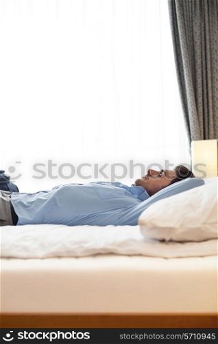 Side view of young businessman sleeping on bed in hotel room