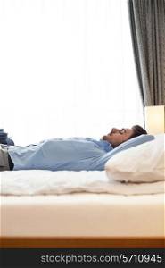 Side view of young businessman sleeping on bed in hotel room