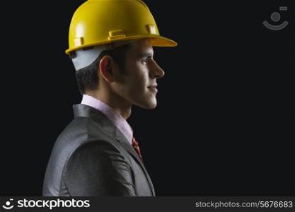 Side view of young businessman wearing hardhat against black background