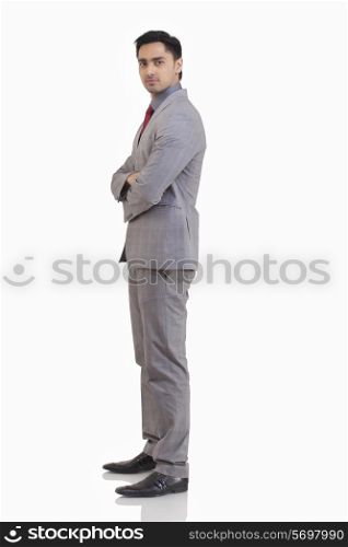Side view of young businessman with arms crossed standing against white background