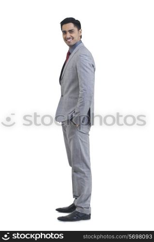 Side view of young businessman with hand in pocket standing against white background
