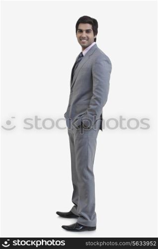 Side view of young businessman with hands in pockets standing against white background