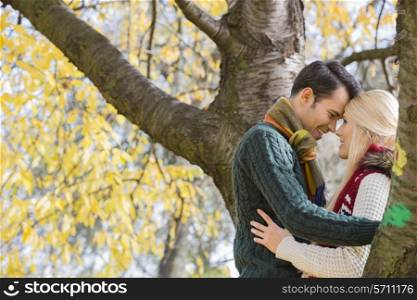 Side view of young couple hugging near autumn tree in park