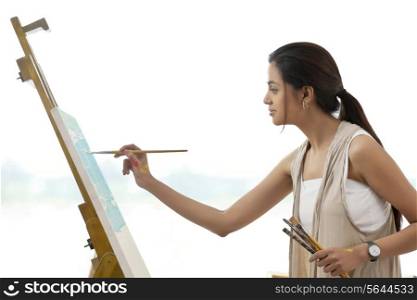 Side view of young female artist painting on canvas isolated over white background