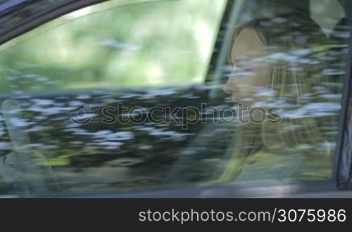 Side view of young female sitting in driver&acute;s seat, putting sunglasses on and fastening seat belt.