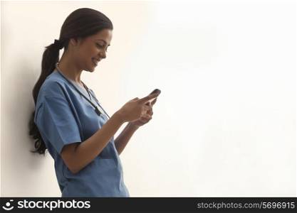 Side view of young female surgeon text messaging through cell phone isolated over white background