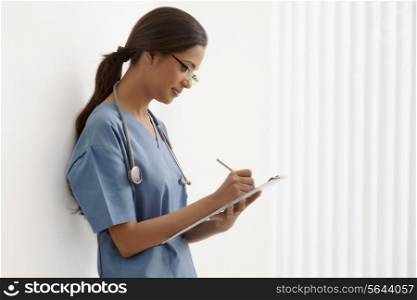 Side view of young female surgeon writing notes while leaning on wall