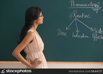 Side view of young female teacher looking at written text on green board
