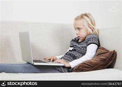 Side view of young girl using laptop on sofa