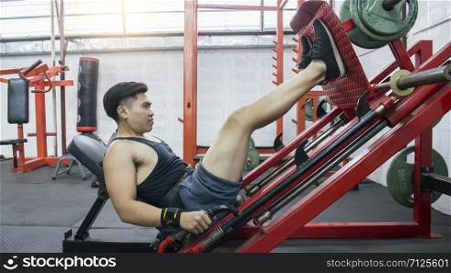 Side view of young handsome asian man doing leg presses in health fitness center