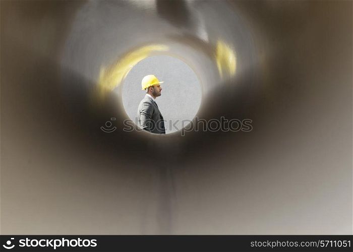 Side view of young male architect through large pipe at construction site