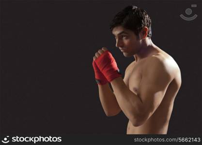 Side view of young male boxer practicing isolated over black background