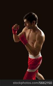Side view of young male boxer standing against black background