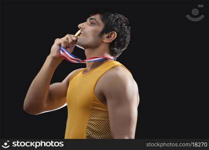 Side view of young male runner kissing medal over black background