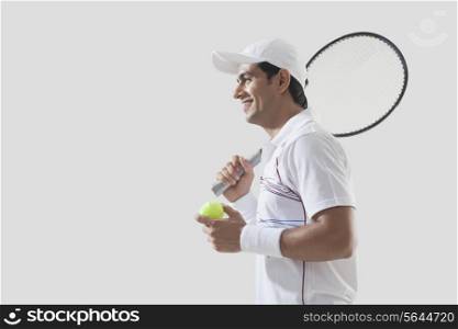 Side view of young man holding tennis racket and ball isolated over gray background