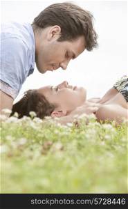 Side view of young man looking at woman sleeping on grass against sky