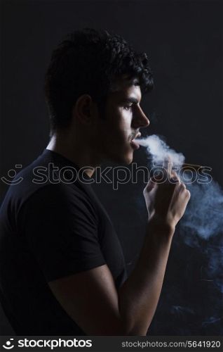 Side view of young man smoking against black background
