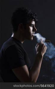 Side view of young man smoking against black background
