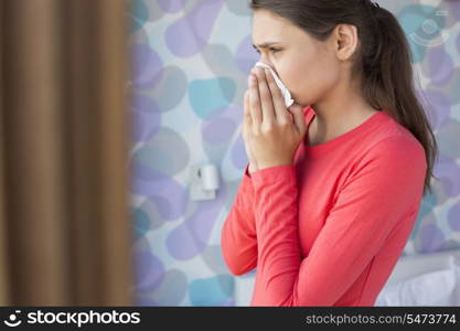 Side view of young woman blowing nose at home