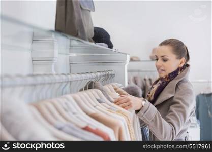 Side view of young woman choosing sweater in store