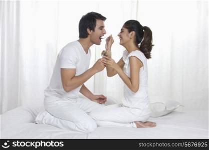 Side view of young woman feeding man chocolate ice cream in bed