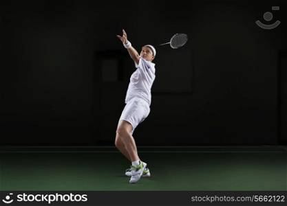 Side view of young woman in sportswear playing badminton isolated over black background
