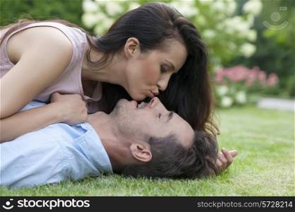 Side view of young woman kissing man while lying in park