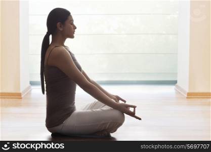 Side view of young woman meditating on floor