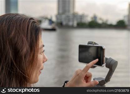 Side view of young woman standing by river and filming vdo on smartphone. Filming or shooting concept.