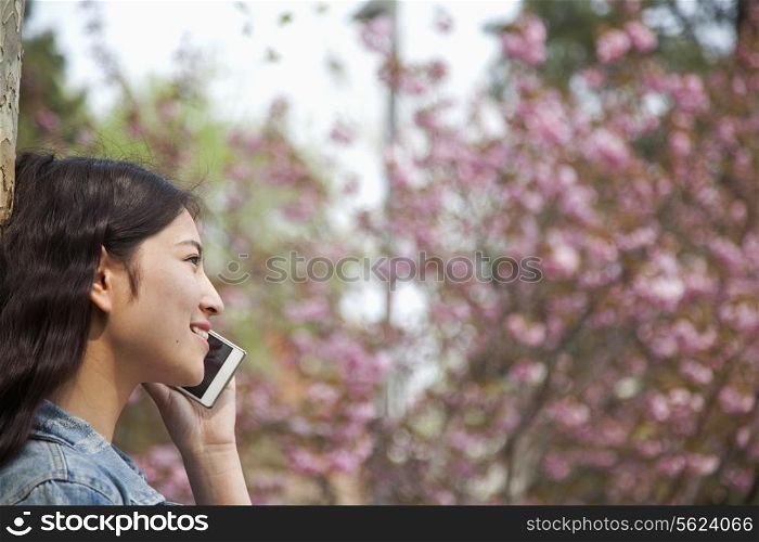 Side view of young woman talking on the phone outdoors in the park in springtime