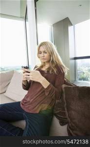 Side view of young woman text messaging at home