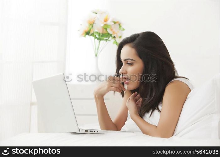 Side view of young woman using laptop in bed