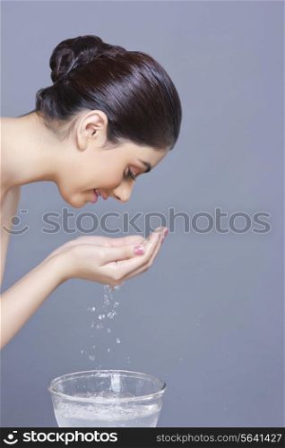 Side view of young woman washing face with water against blue background